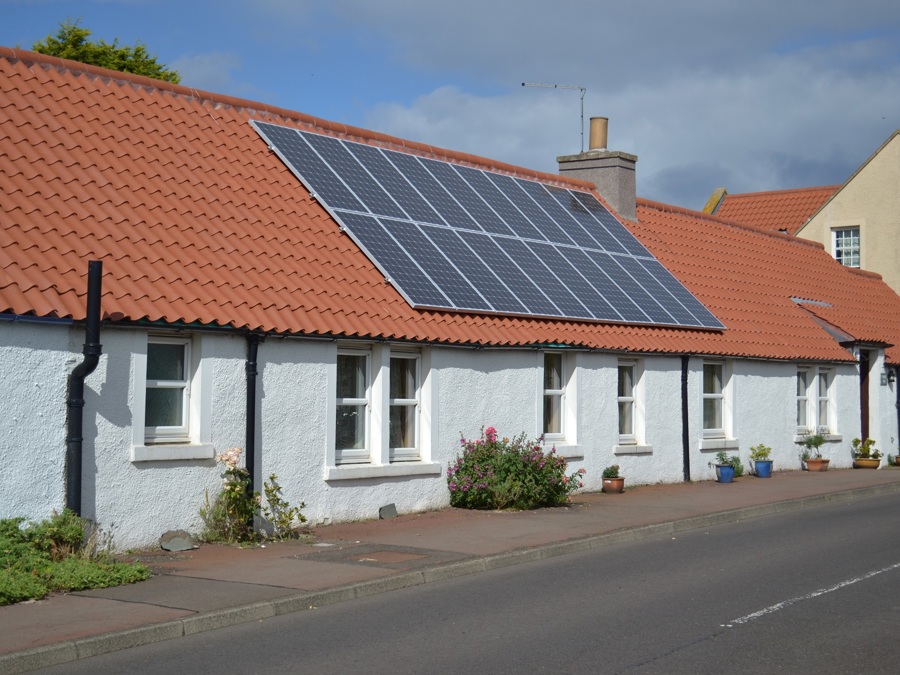 A row of traditional lime harled cottages with solar panels on a pantile roof
